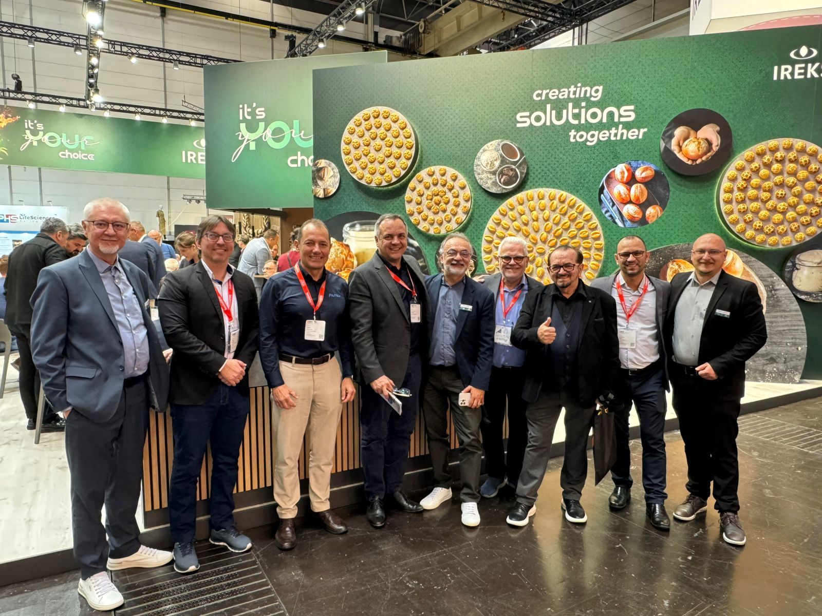 Um grupo de homens está posando para uma foto em frente a uma placa que diz `` criando soluções juntos ''.