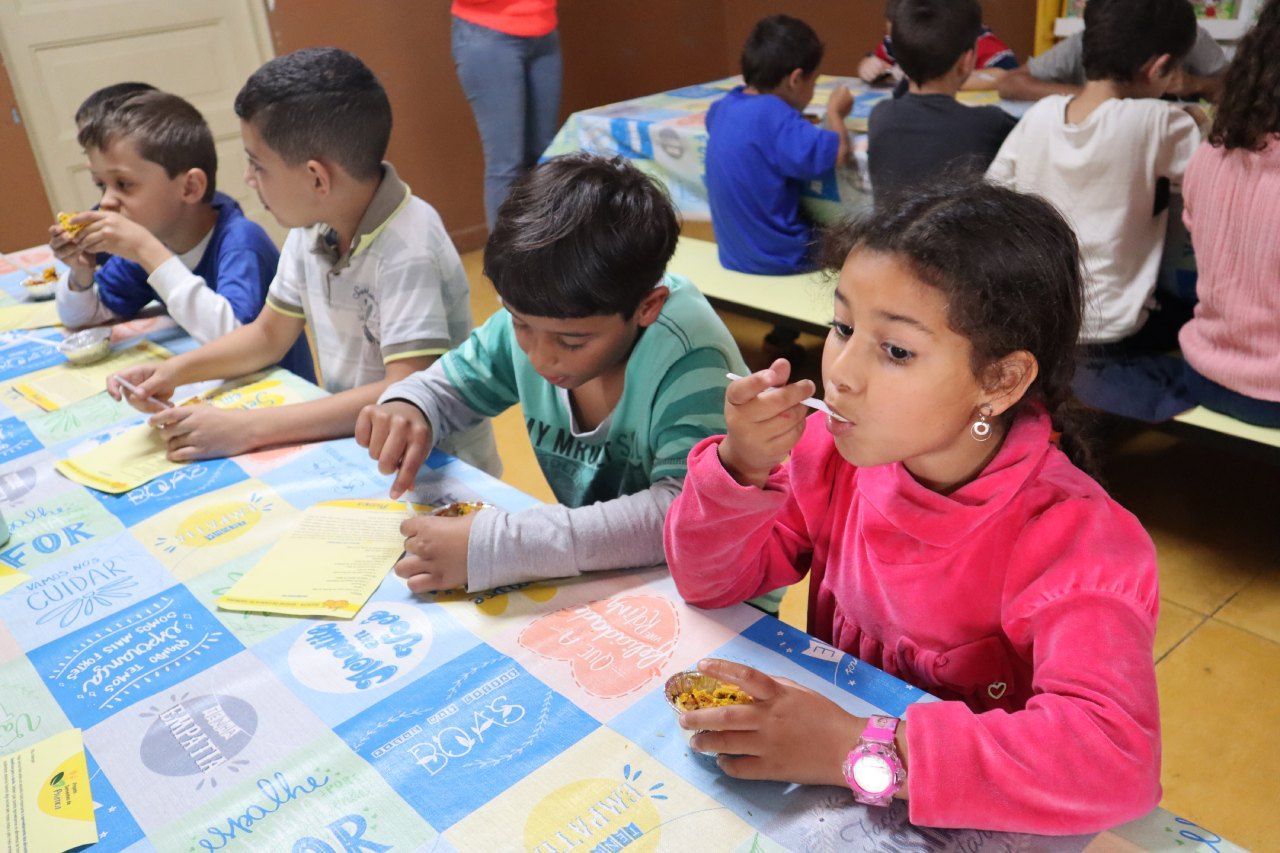 Um grupo de crianças está sentado à mesa comendo.