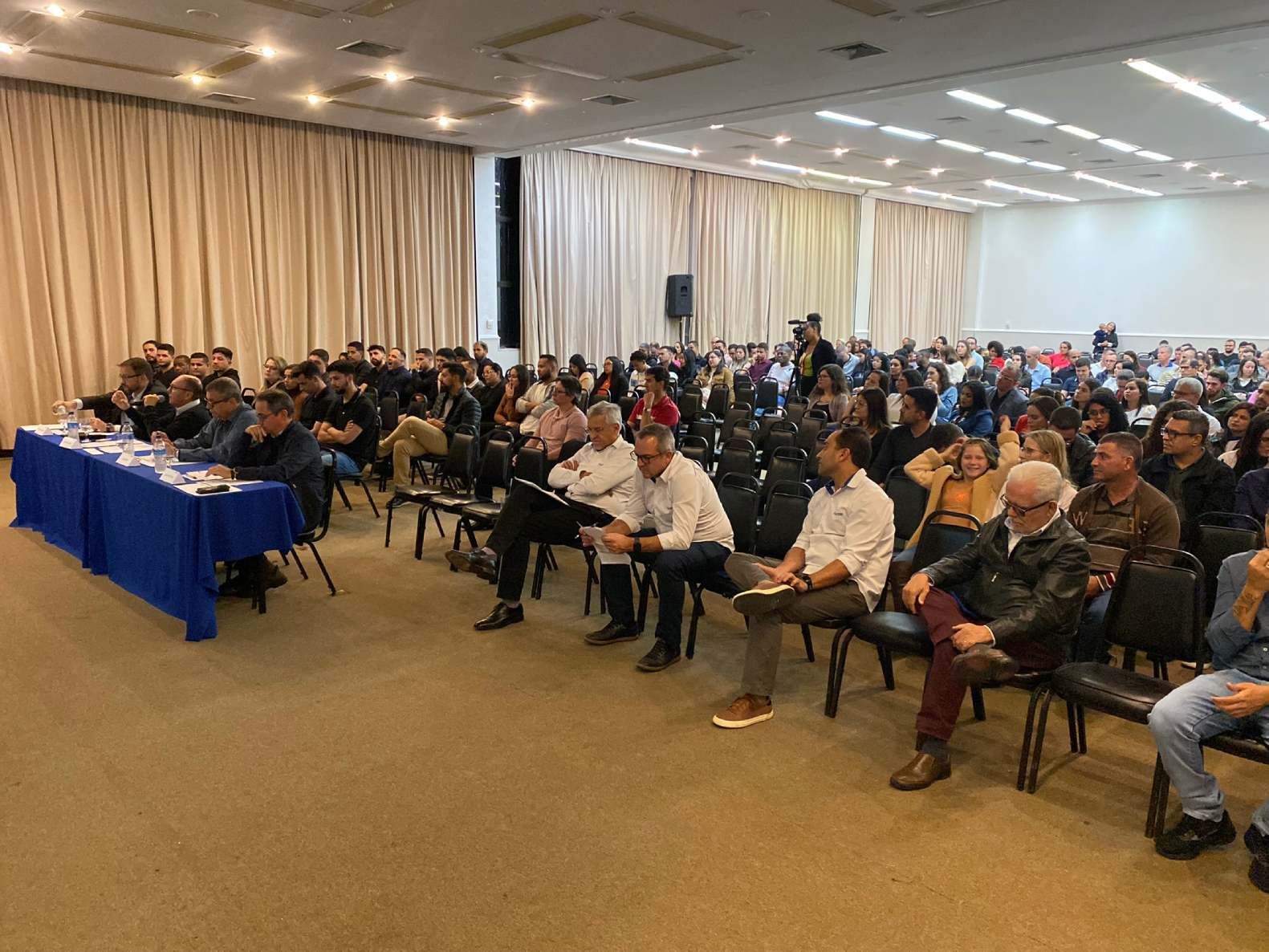 Um grande grupo de pessoas está sentado em uma sala grande.