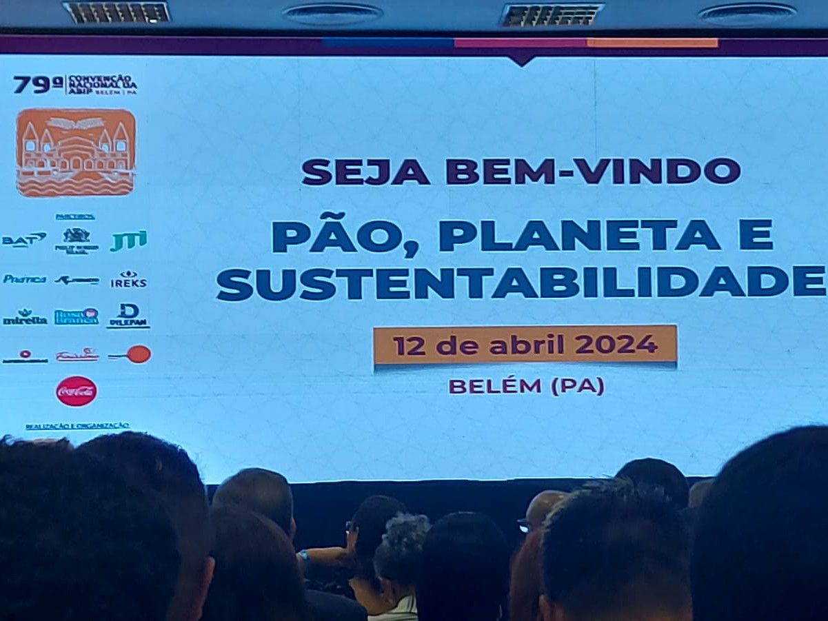A group of people are sitting in front of a large screen that says seja bem-vindo pão planeta e sustentabilidade