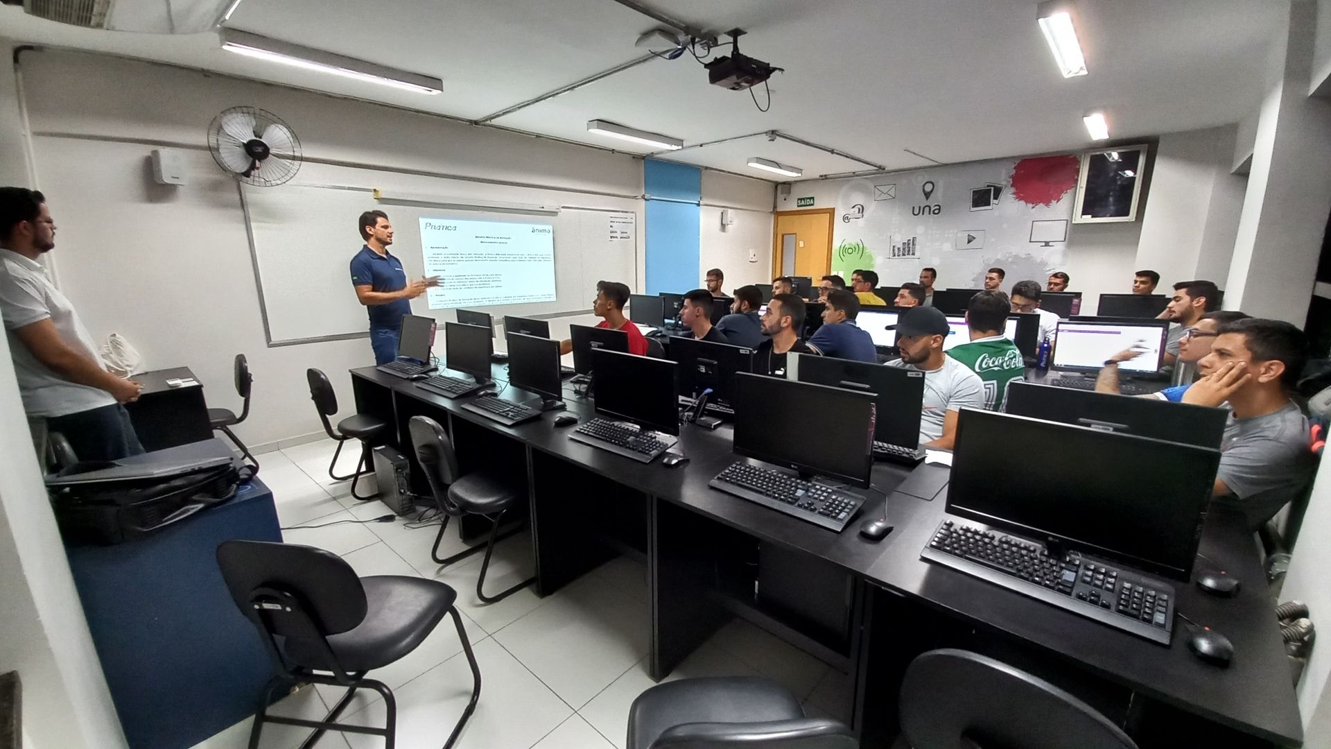 Um homem está fazendo uma apresentação para um grupo de pessoas em um laboratório de informática.