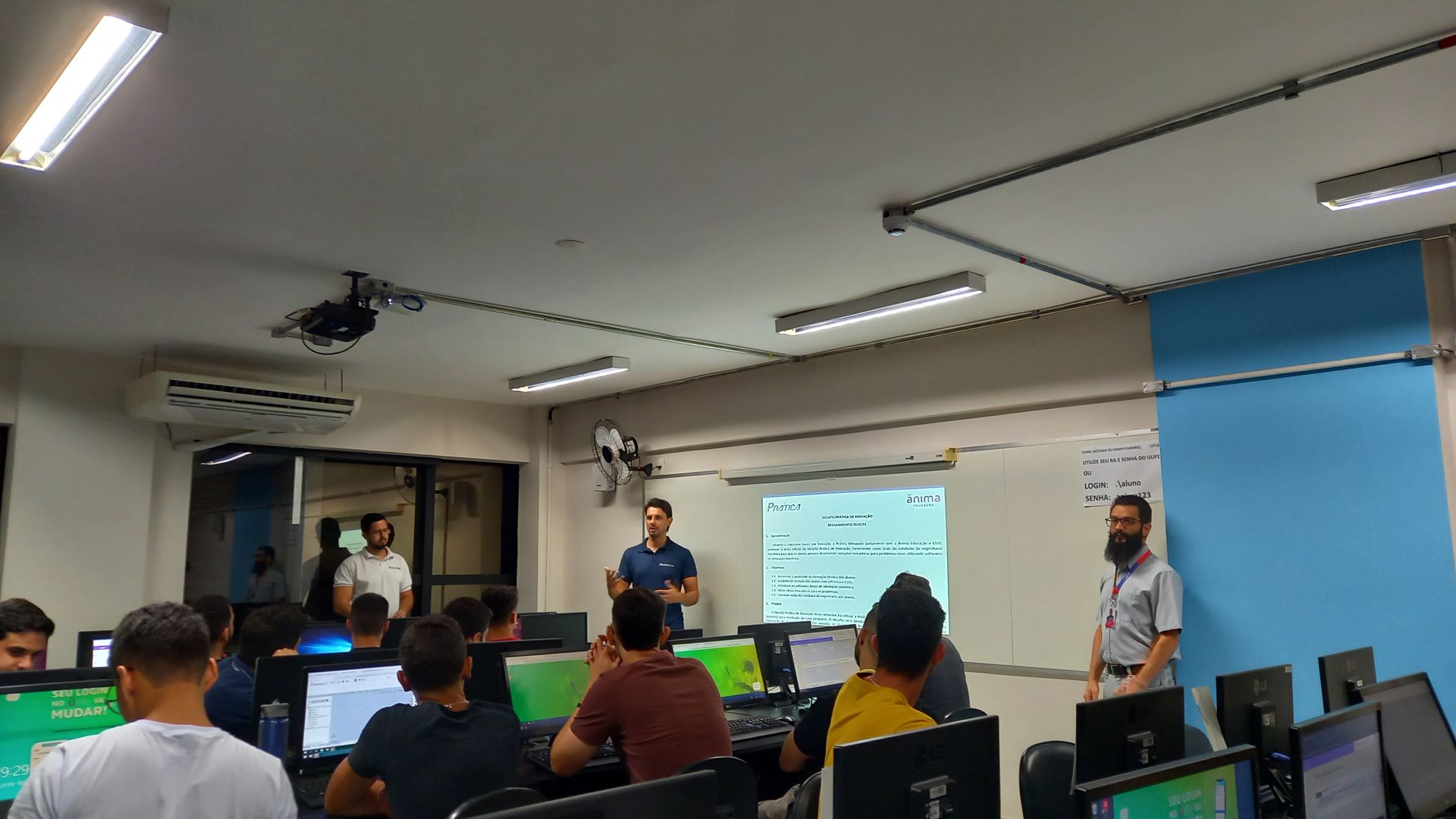 Um grupo de pessoas está sentado em frente aos computadores em uma sala.