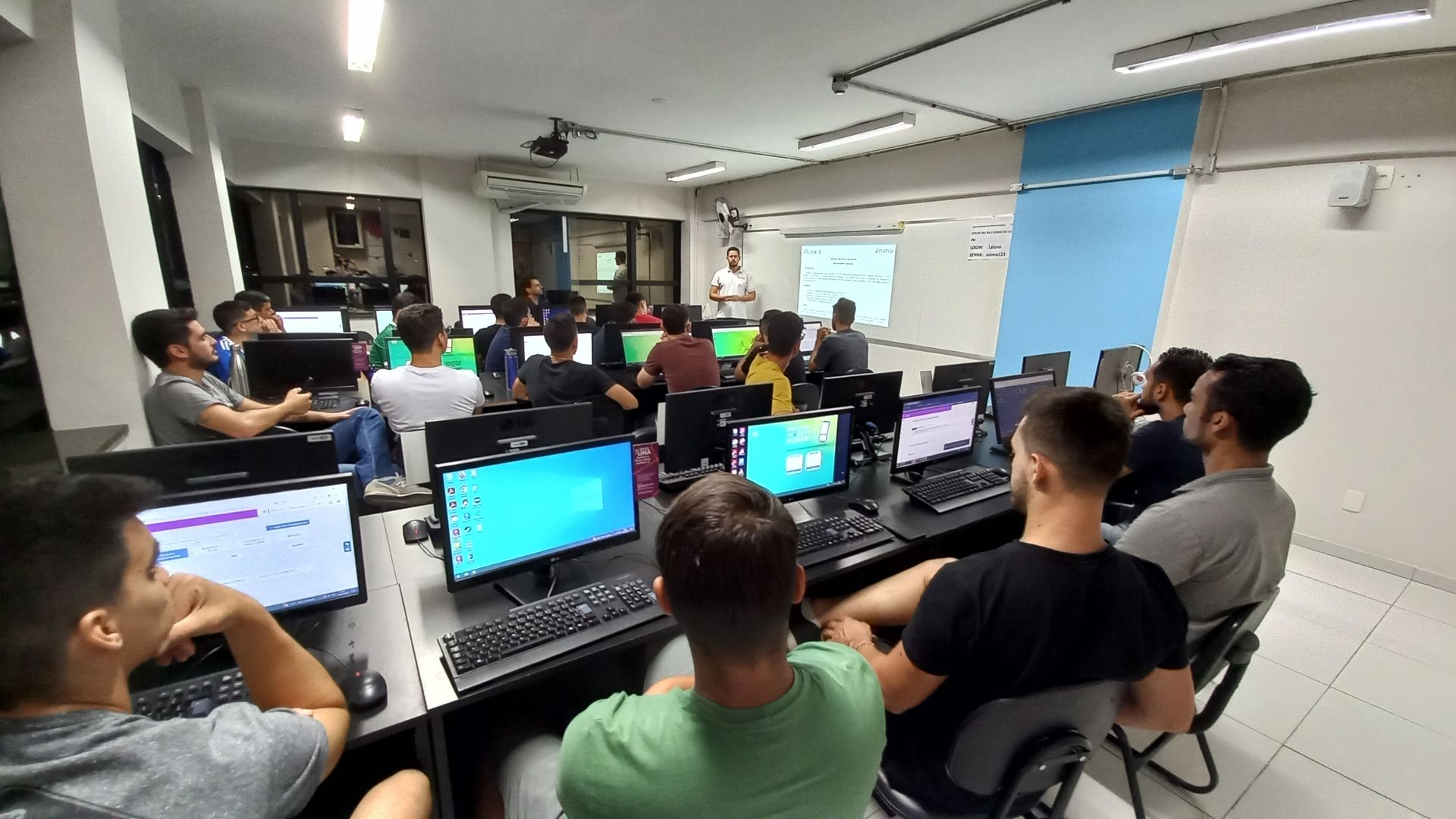 Um grupo de pessoas está sentado em frente aos computadores em uma sala.
