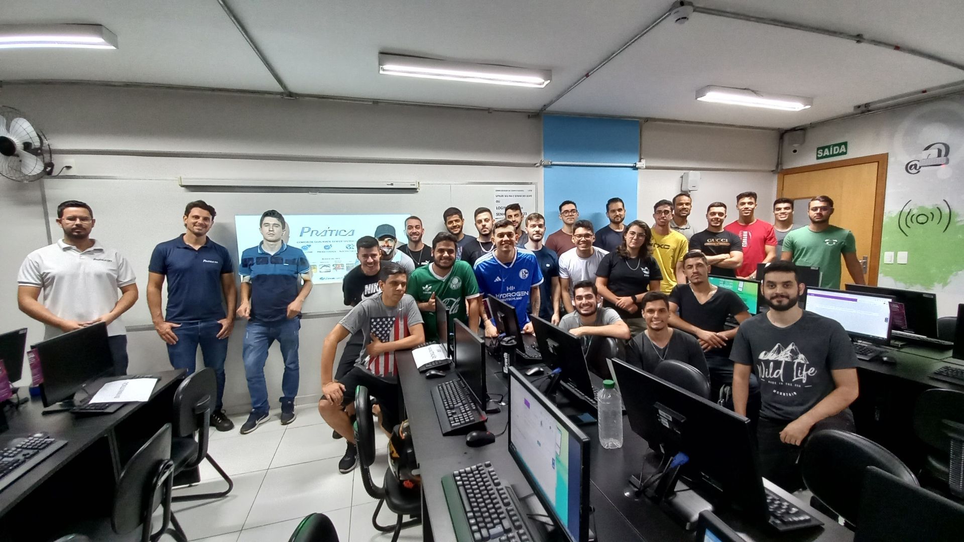 Um grupo de pessoas está posando para uma foto em um laboratório de informática.