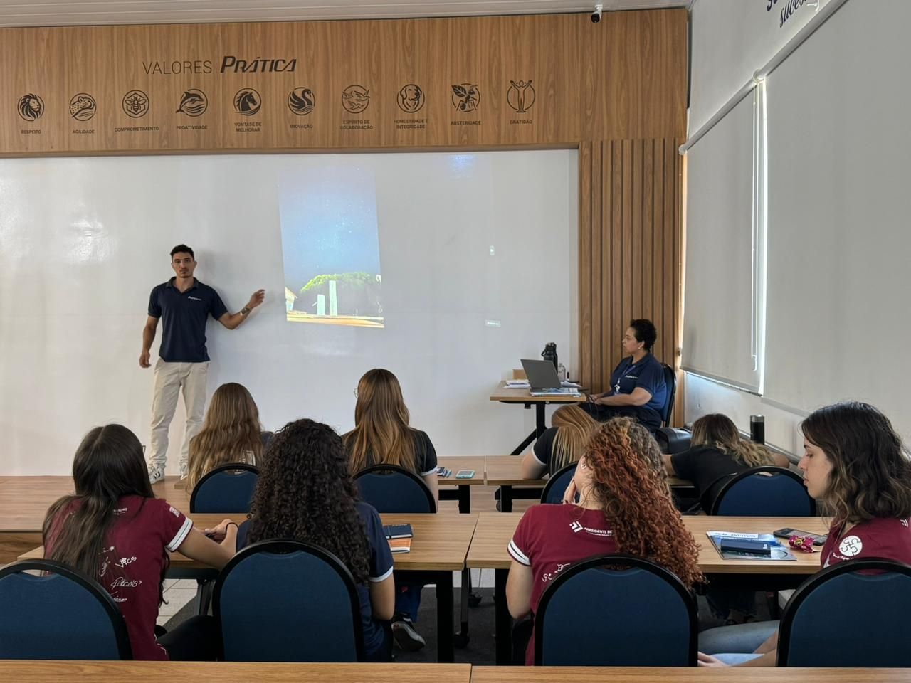 Um homem está fazendo uma apresentação para um grupo de alunos em uma sala de aula.