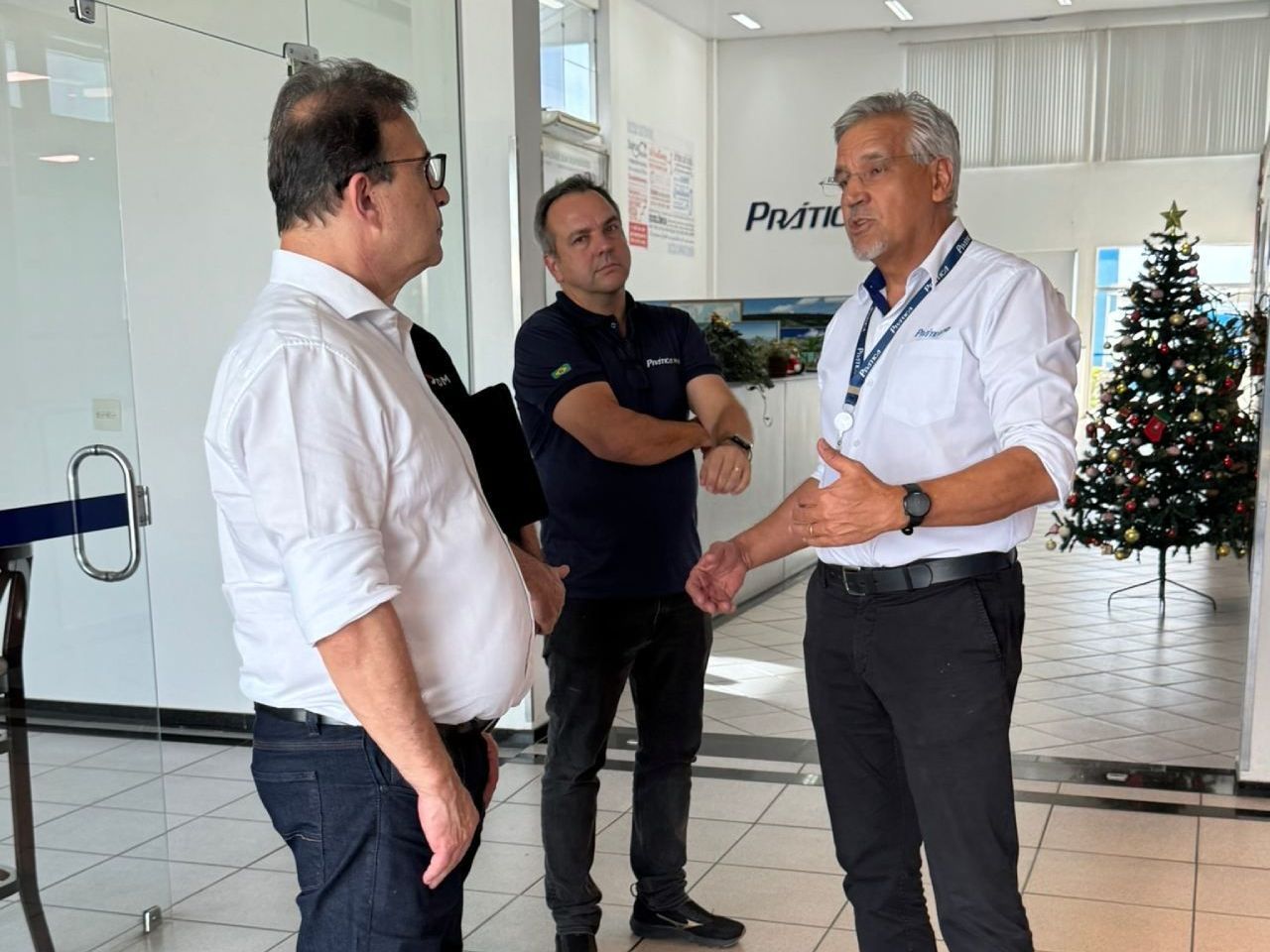 Três homens estão em pé em uma sala com uma árvore de natal ao fundo.