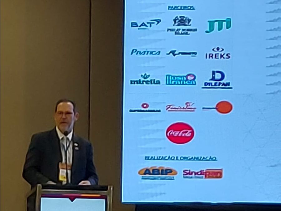 Um homem está em um pódio em frente a uma tela grande com logotipos nela