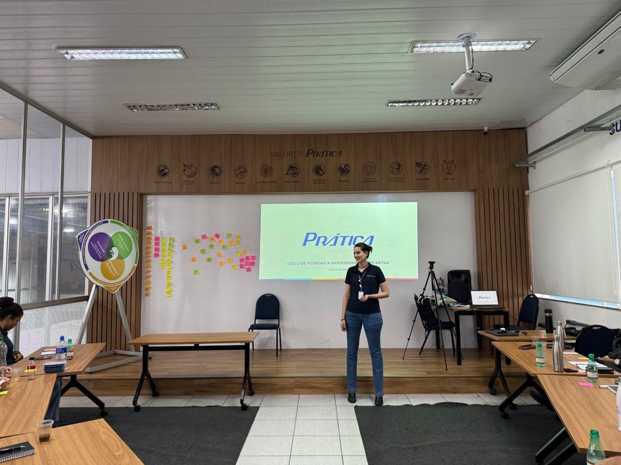Uma pessoa está em um palco em frente a uma tela de projeção com a inscrição 