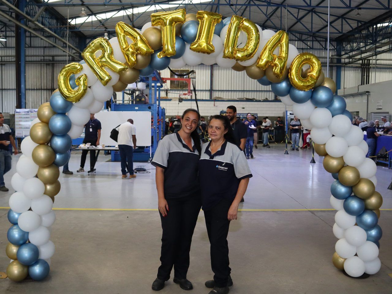 Duas mulheres estão de pé sob um arco de balões que diz gratidao