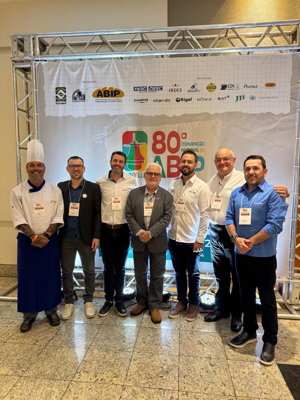 Um grupo de homens está posando para uma foto em frente a uma placa.