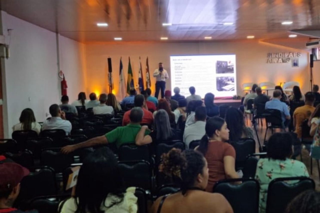 Um grande grupo de pessoas está sentado em um auditório assistindo a uma apresentação.