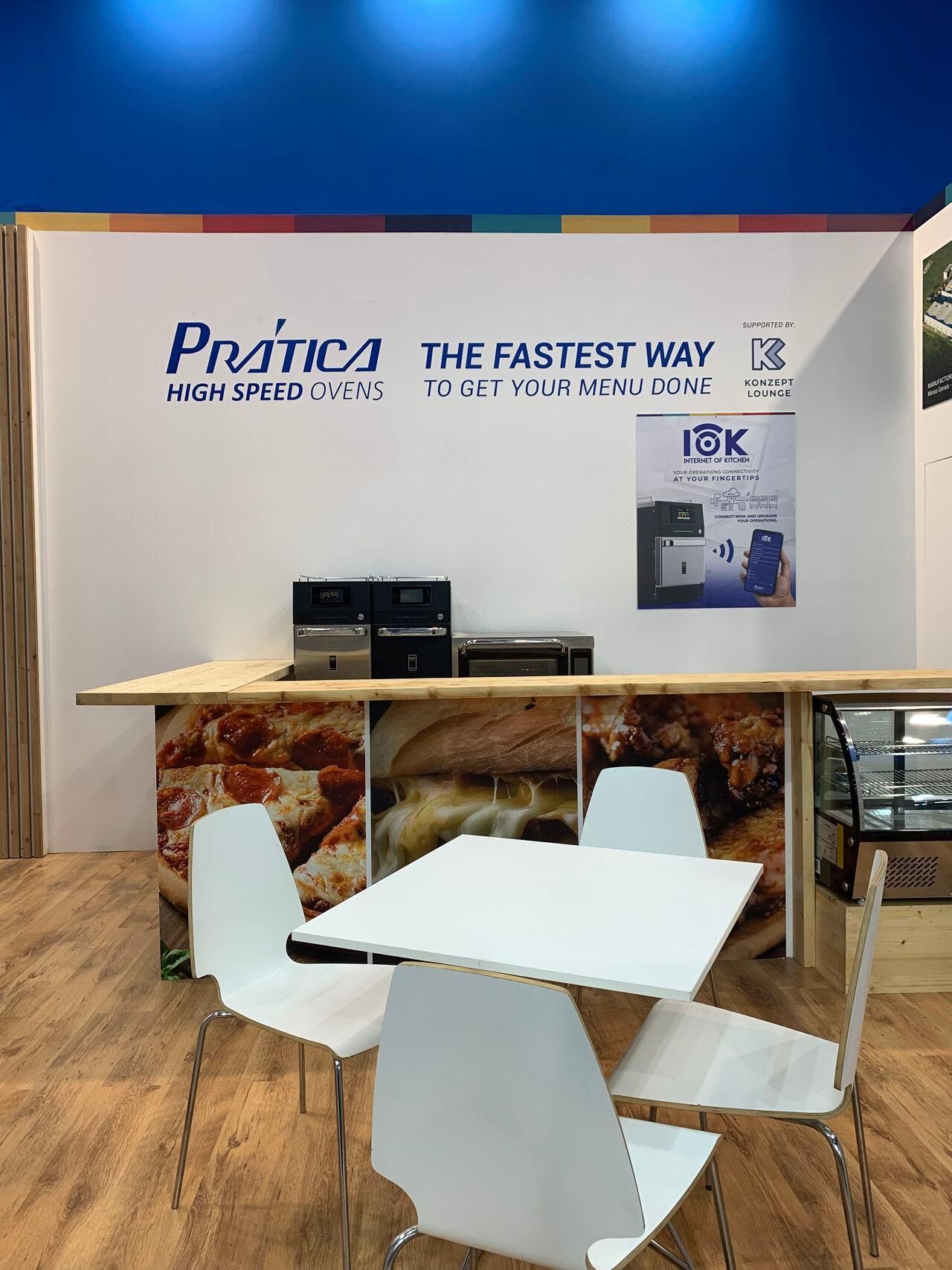 Há uma mesa e cadeiras em frente a um balcão com pizza em cima.