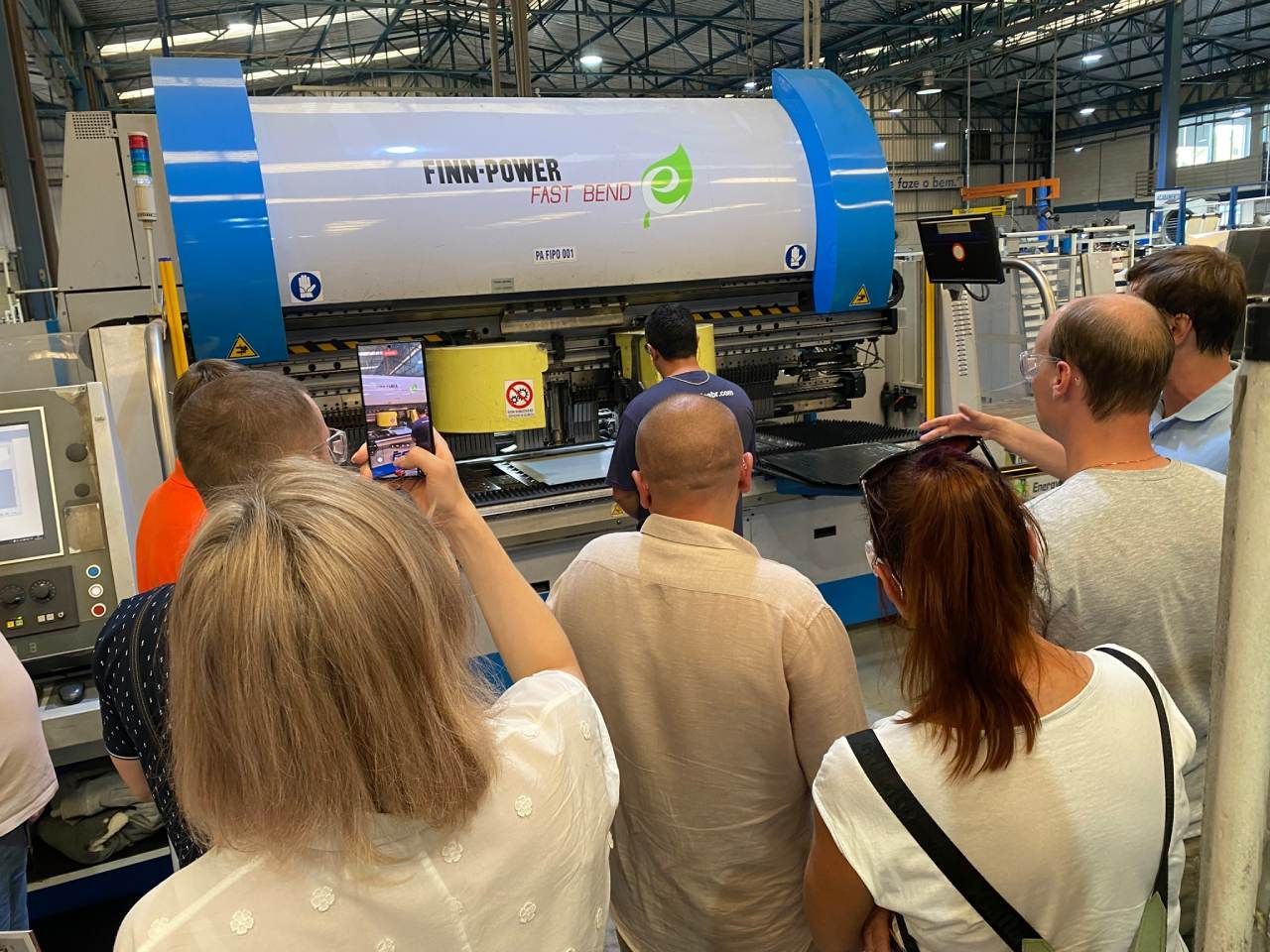 Um grupo de pessoas está em volta de uma máquina em uma fábrica.