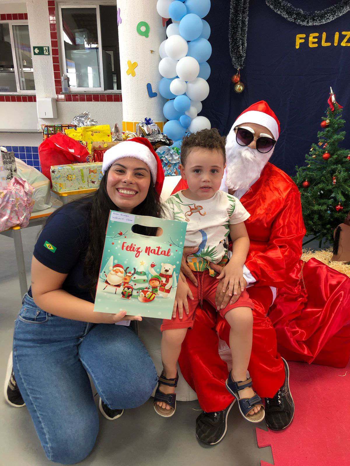 Uma mulher está ajoelhada ao lado de uma criança vestida de Papai Noel.