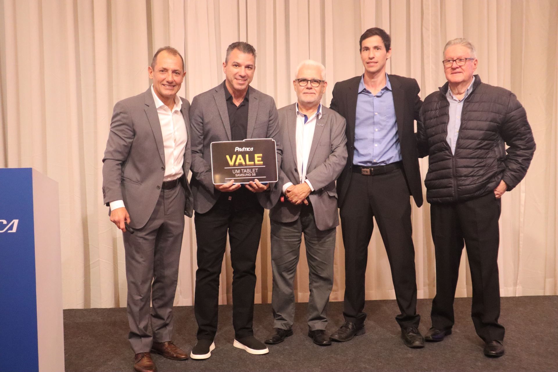 Um grupo de homens está de pé, um ao lado do outro, segurando uma placa que diz vale.