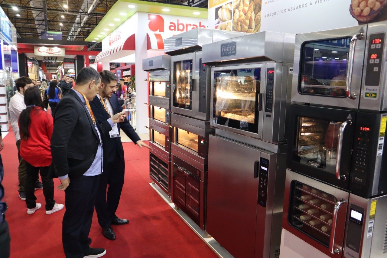 Um grupo de pessoas está em pé em frente a uma fileira de fornos.