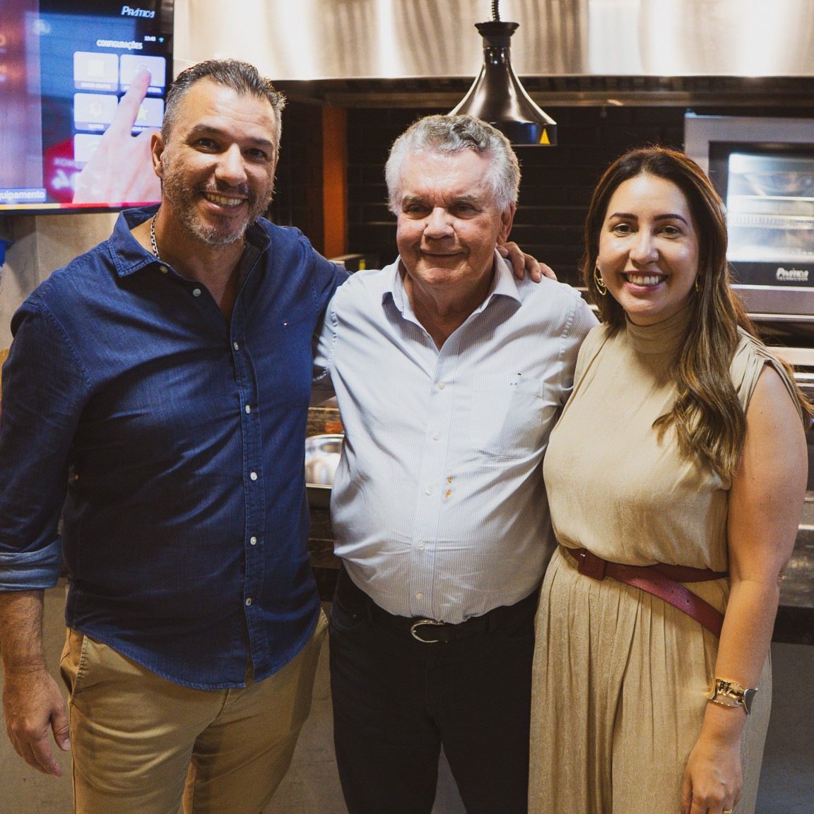 Dois homens e uma mulher estão posando para uma foto em uma cozinha