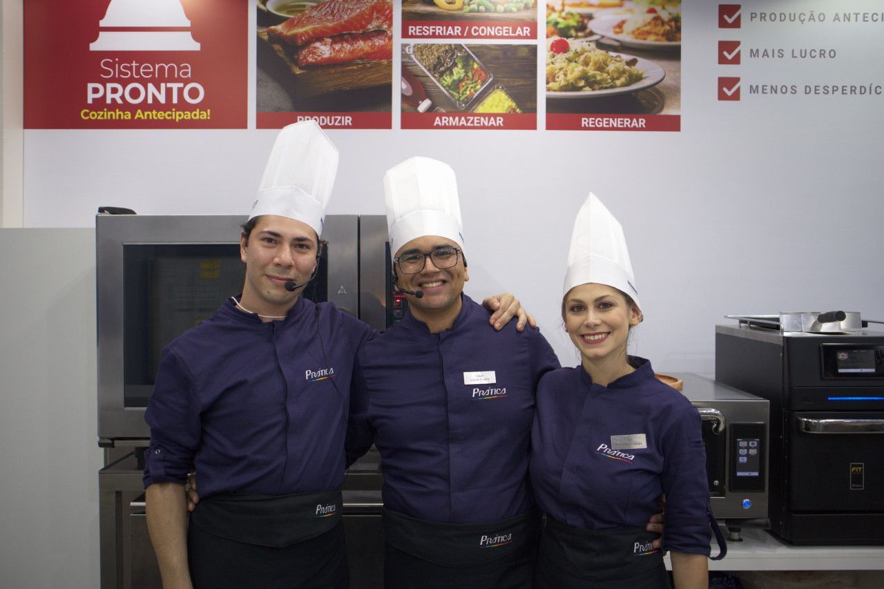 Três chefs estão posando para uma foto em frente a uma placa que diz pronto