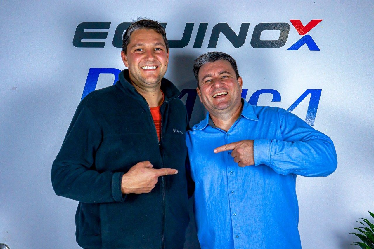 Dois homens estão posando para uma foto em frente a uma placa que diz equinócio