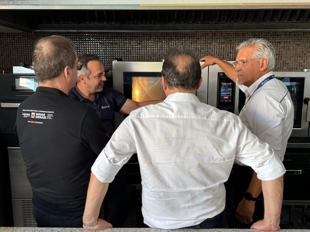 Um grupo de homens está olhando para um micro-ondas em uma cozinha.