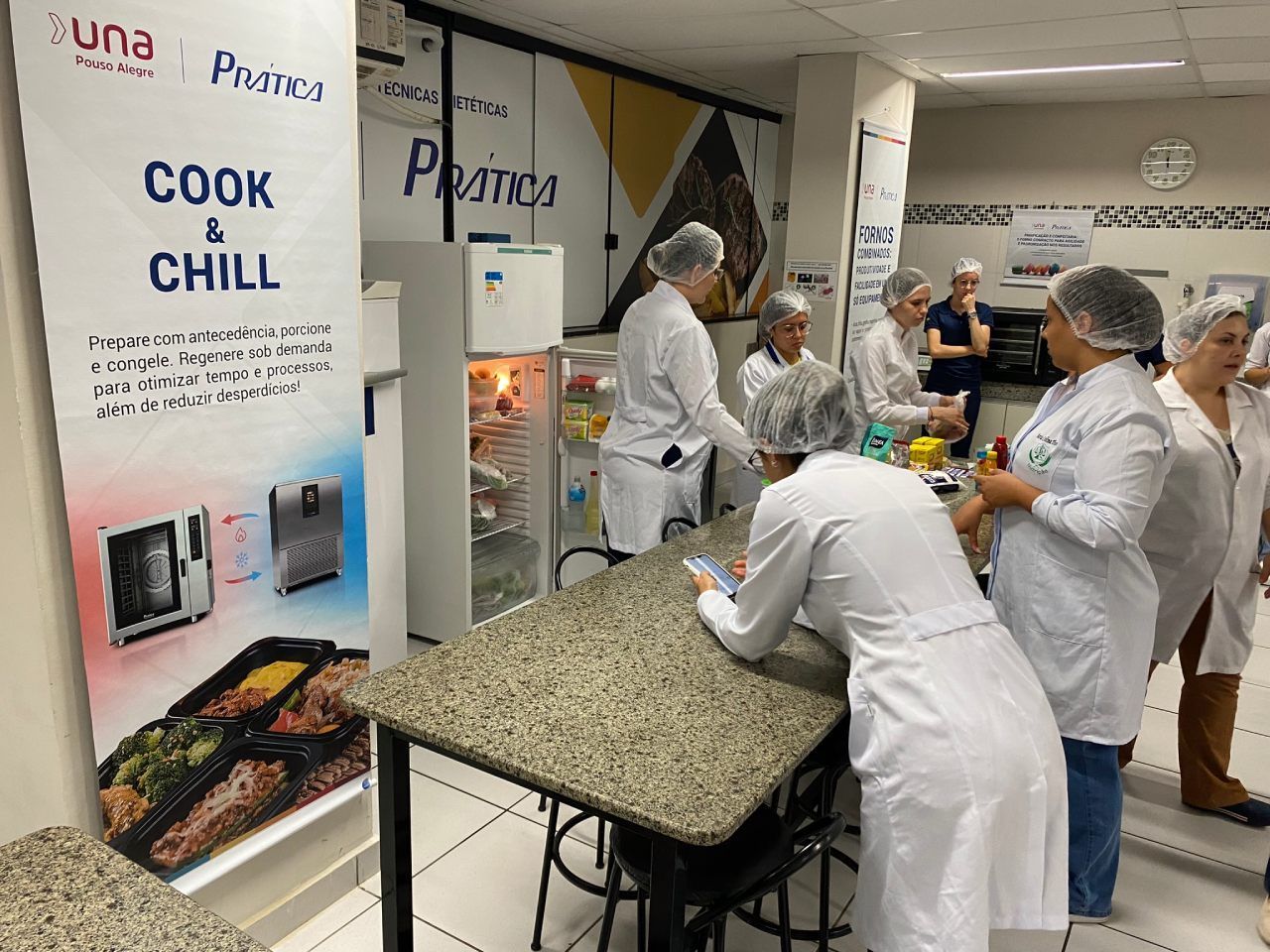 Um grupo de pessoas está em pé ao redor de uma mesa na cozinha.