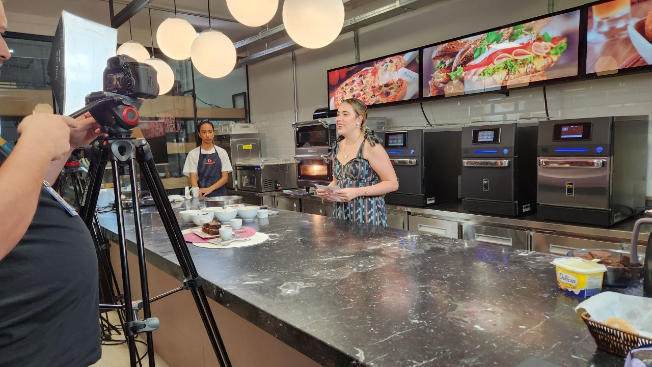 Um homem está tirando uma foto de uma mulher na cozinha com uma câmera.