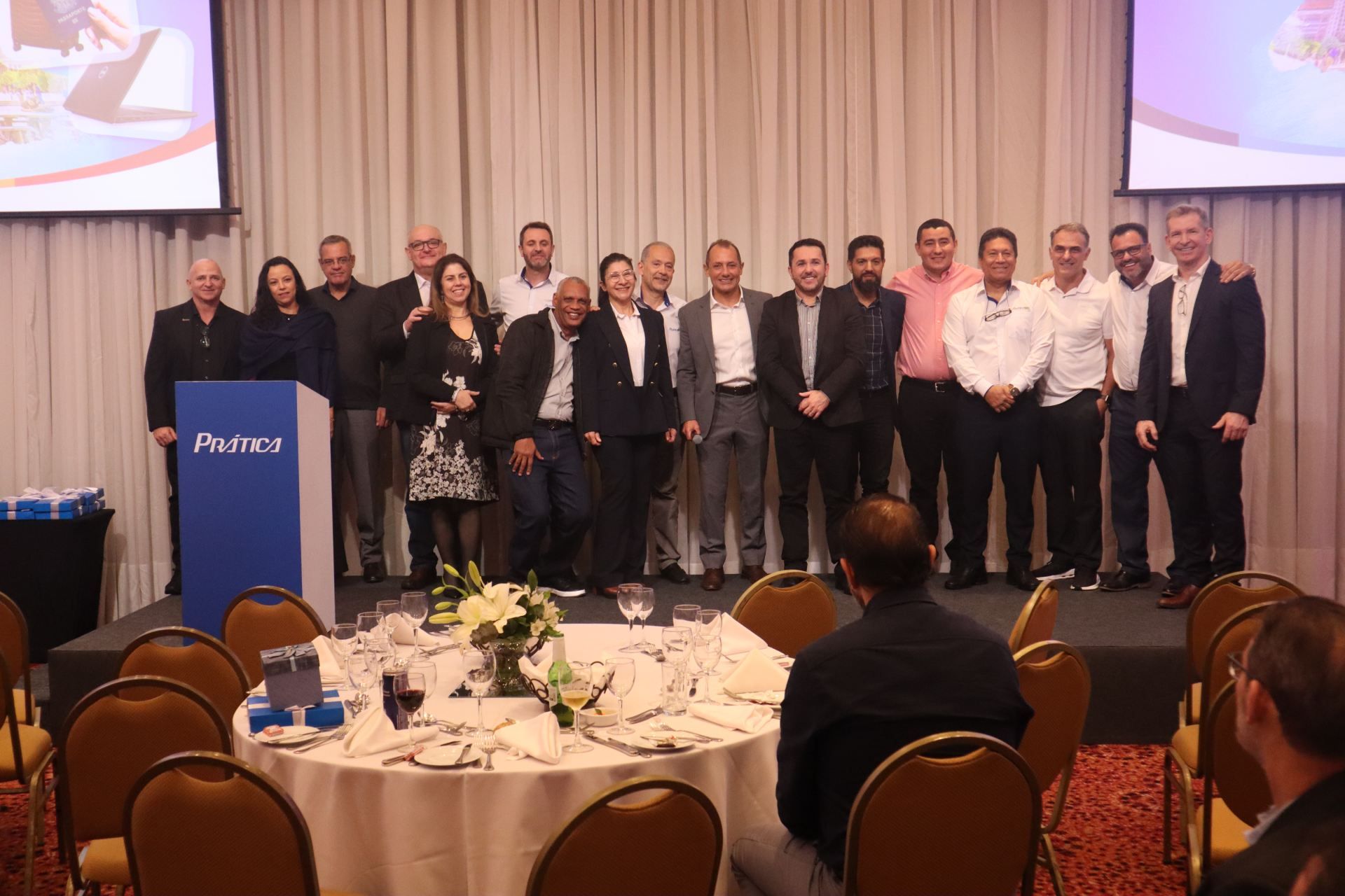 Um grupo de pessoas está posando para uma foto em uma sala com mesas e cadeiras.