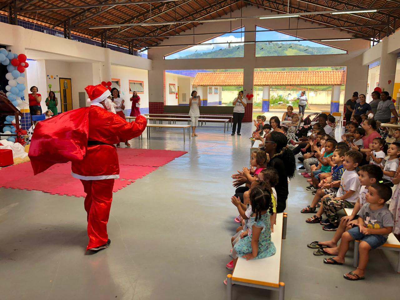 Um homem vestido de papai noel está parado na frente de uma multidão de crianças.