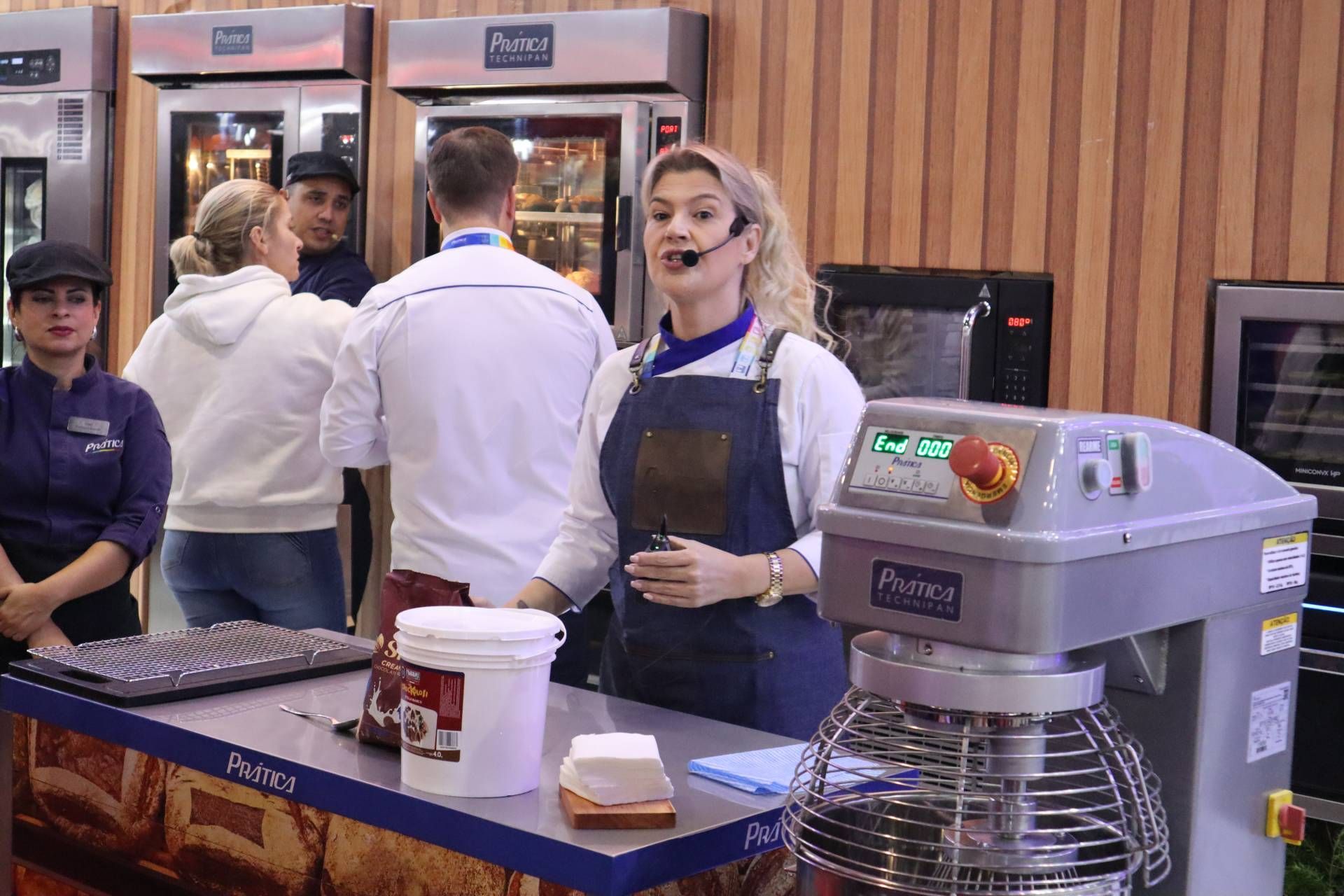 Uma mulher está parada em frente a uma batedeira em uma padaria.
