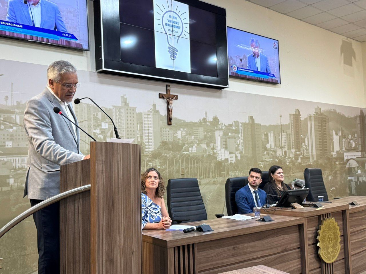 Um homem está em um pódio fazendo um discurso na câmara do conselho.