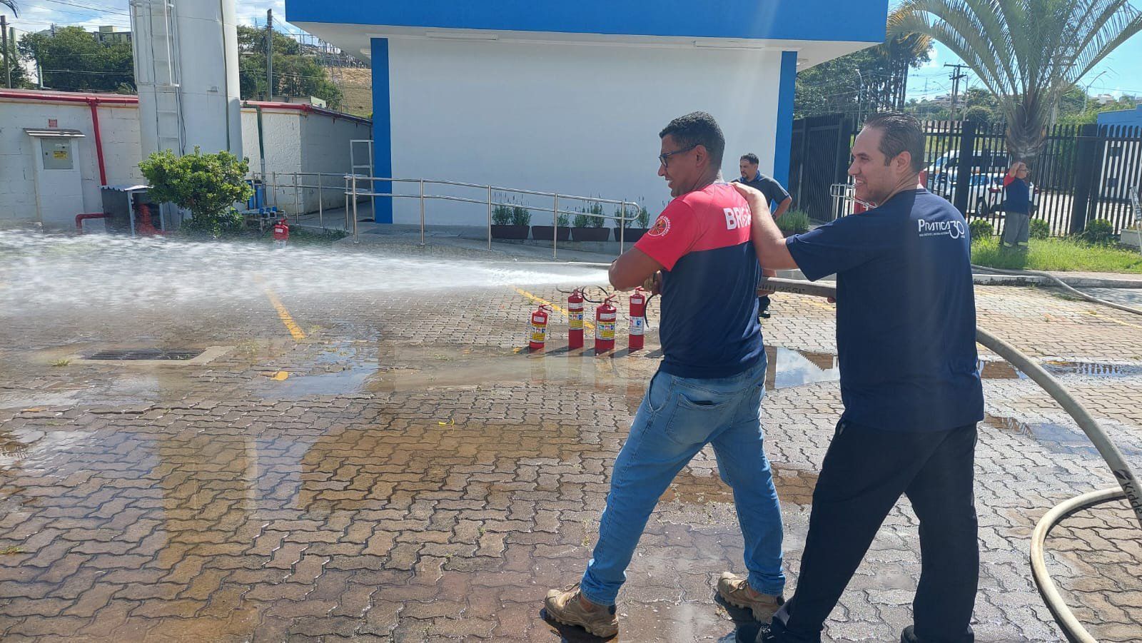 Dois homens estão caminhando em um estacionamento com uma mangueira de incêndio.