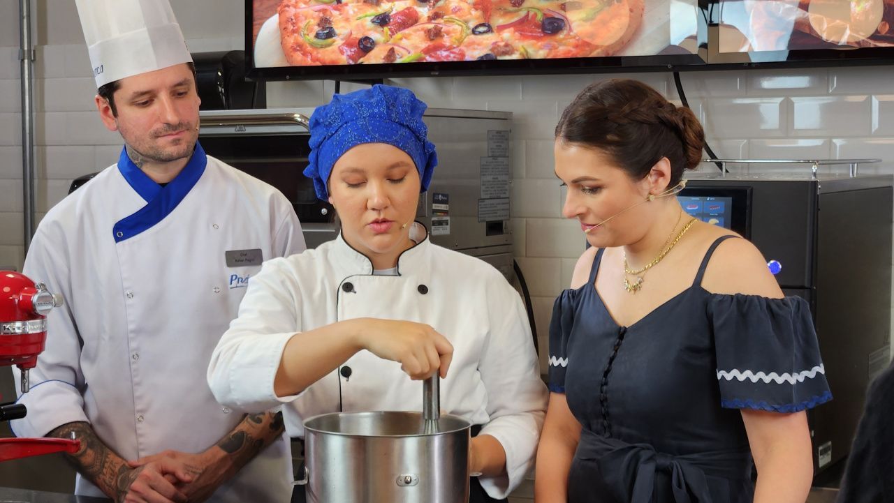Um chef está ensinando uma mulher a fazer pizza na cozinha.