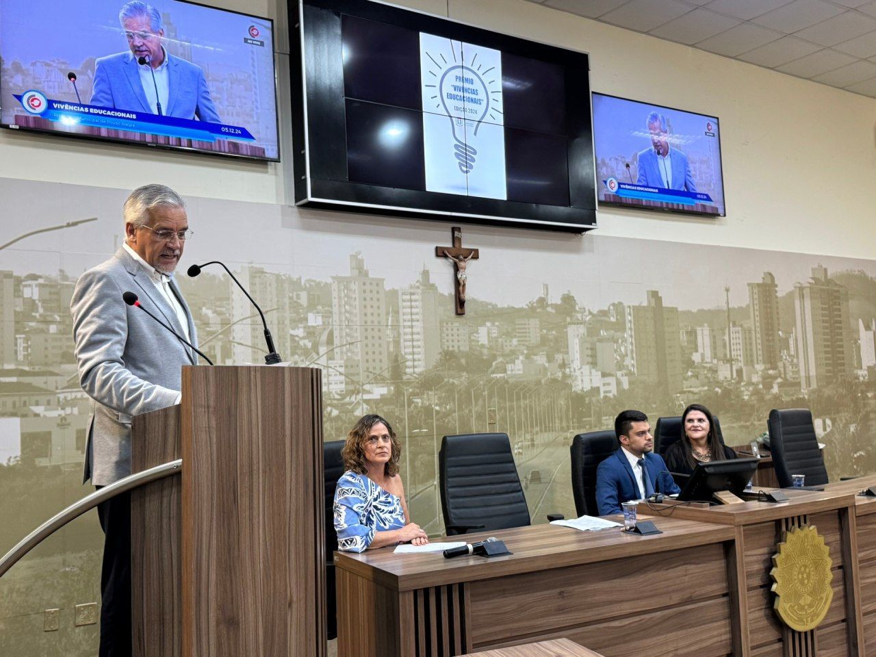 Um homem está em um pódio fazendo um discurso na câmara do conselho.