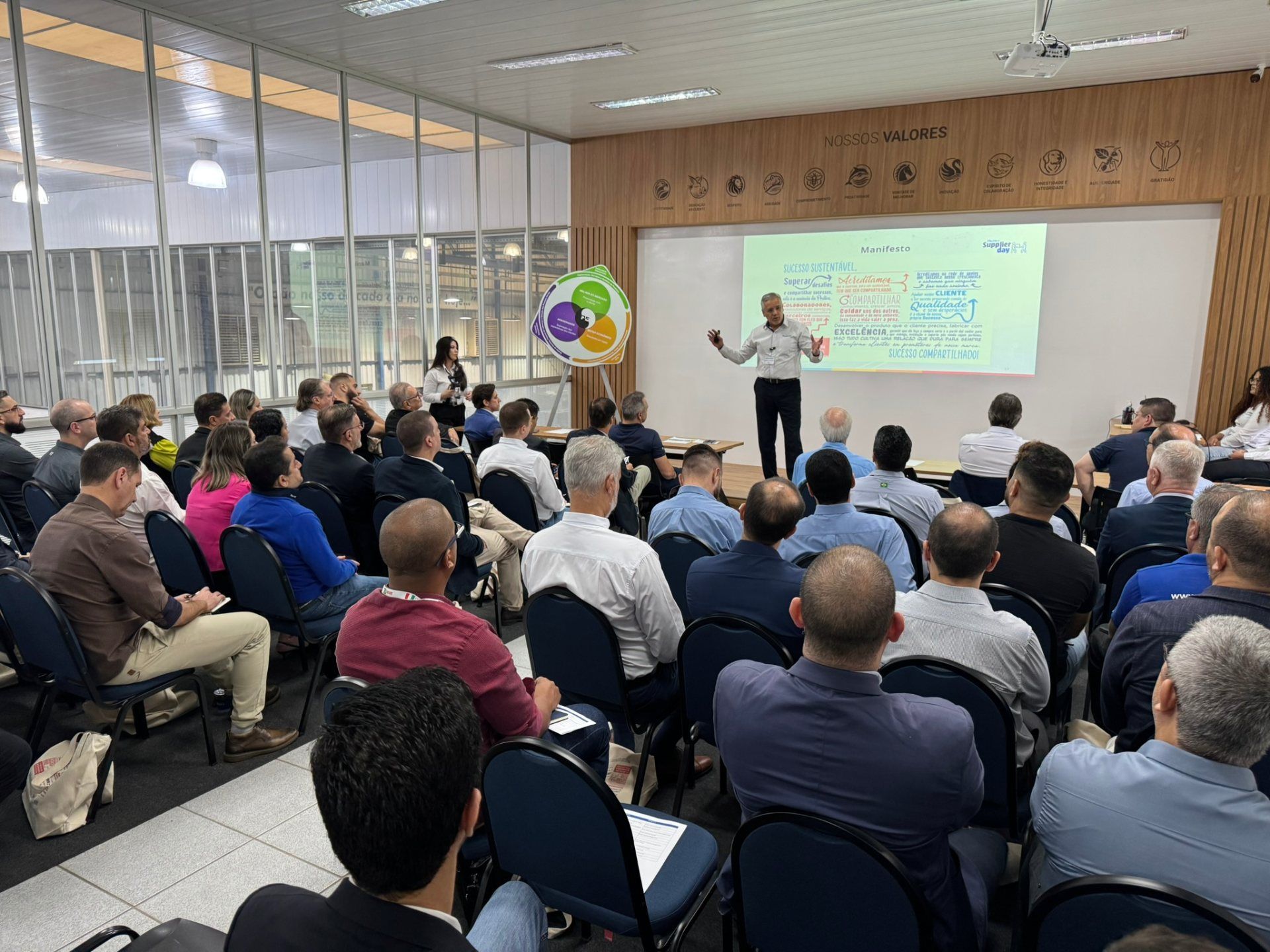 Um grupo de pessoas está sentado em cadeiras em frente a uma tela de projetor.