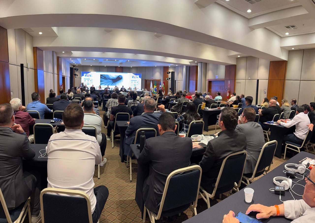 Um grande grupo de pessoas está sentado em mesas em uma sala de conferências.