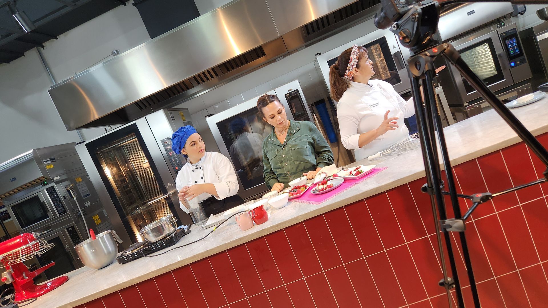 Três chefs estão em frente a uma câmera em uma cozinha.