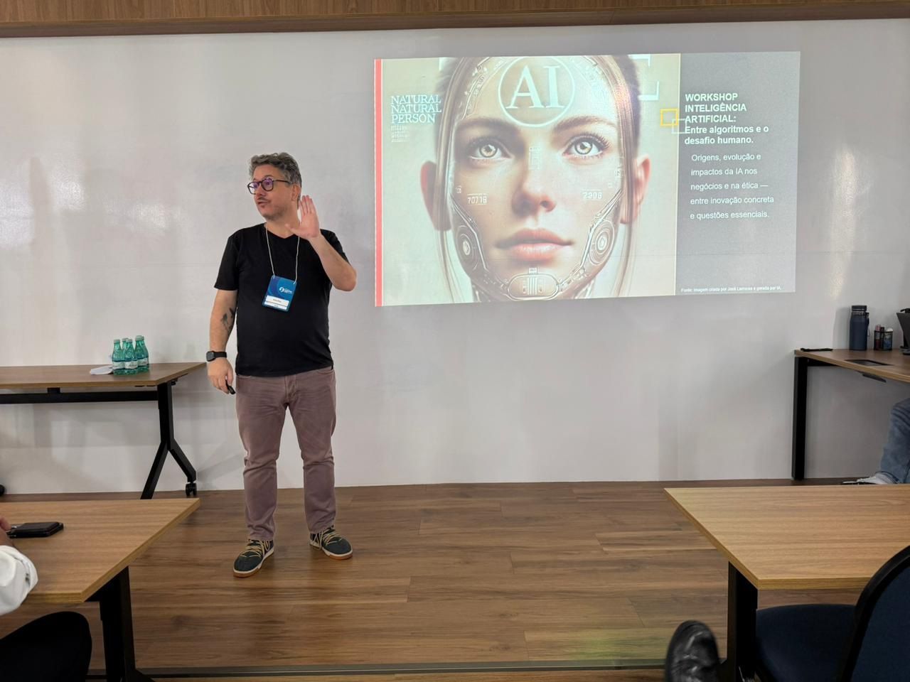 Um homem de camisa preta faz uma apresentação para um grupo, gesticulando em direção a um projetor que exibe uma imagem de IA de uma mulher.