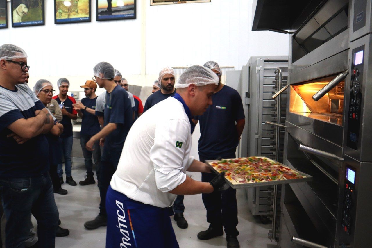 Um homem de camisa branca com a palavra náutica no short está colocando uma pizza no forno