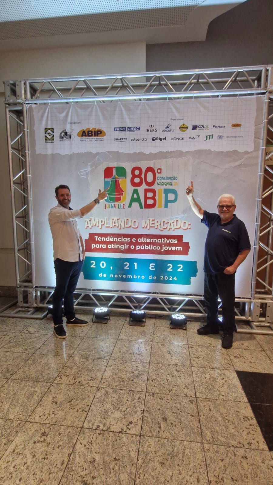 Dois homens estão em pé na frente de uma grande faixa.