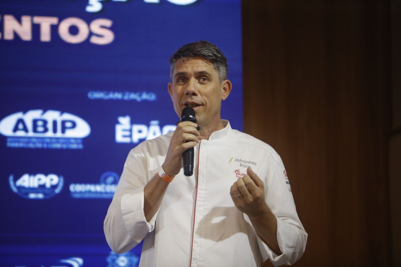 Um homem segura um microfone em frente a uma placa que diz abip