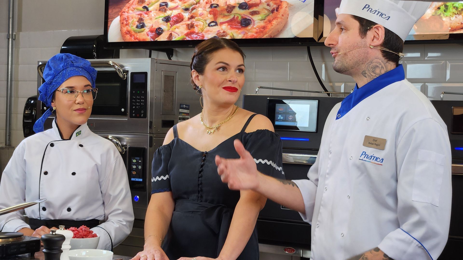 Um homem com uniforme de chef está conversando com duas mulheres na cozinha.