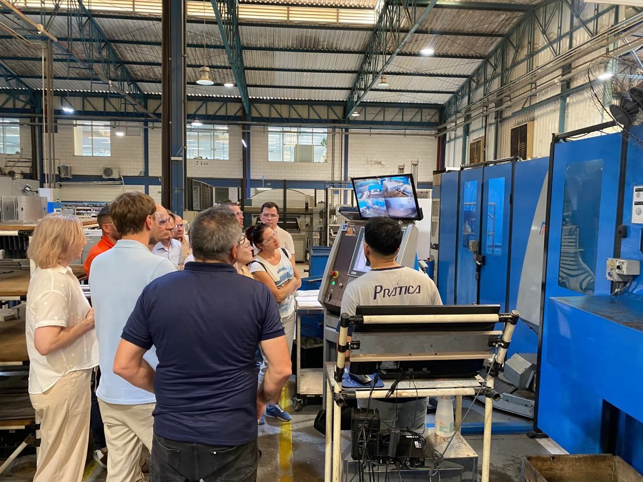 Um grupo de pessoas está em uma fábrica olhando para uma máquina.