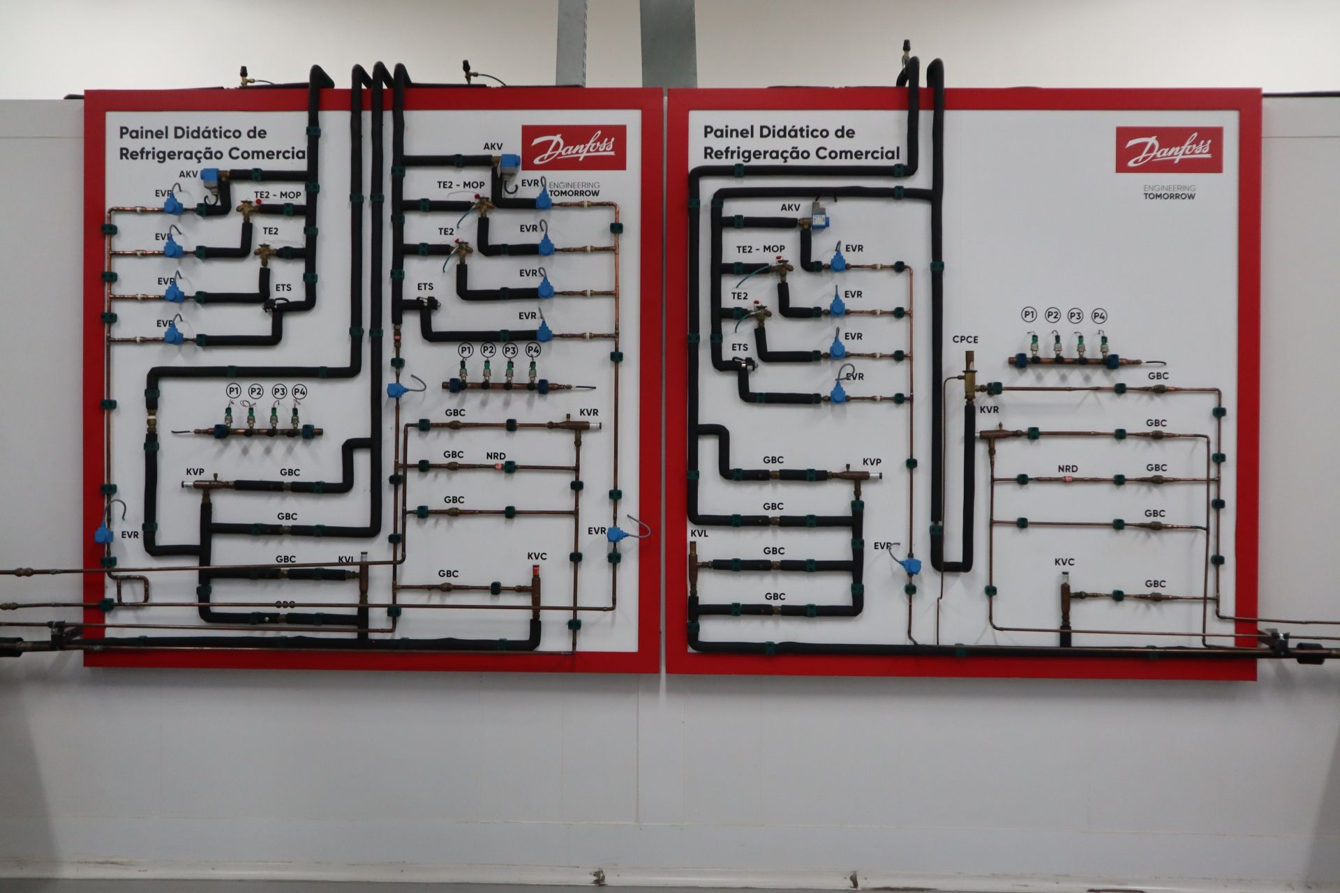 Dois painéis com moldura vermelha e tubulações, válvulas e componentes complexos em preto, provavelmente para demonstração de um sistema mecânico.