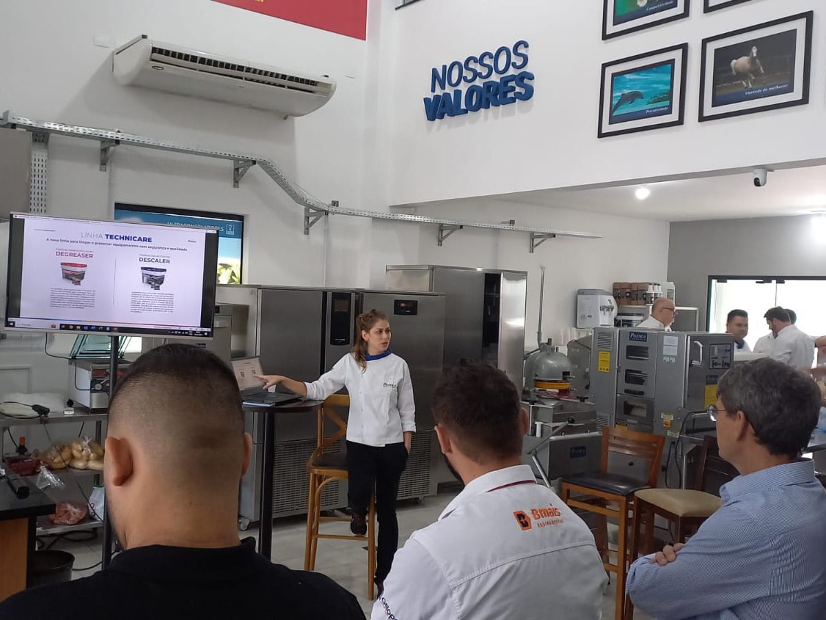 Uma mulher está fazendo uma apresentação para um grupo de pessoas em uma cozinha.