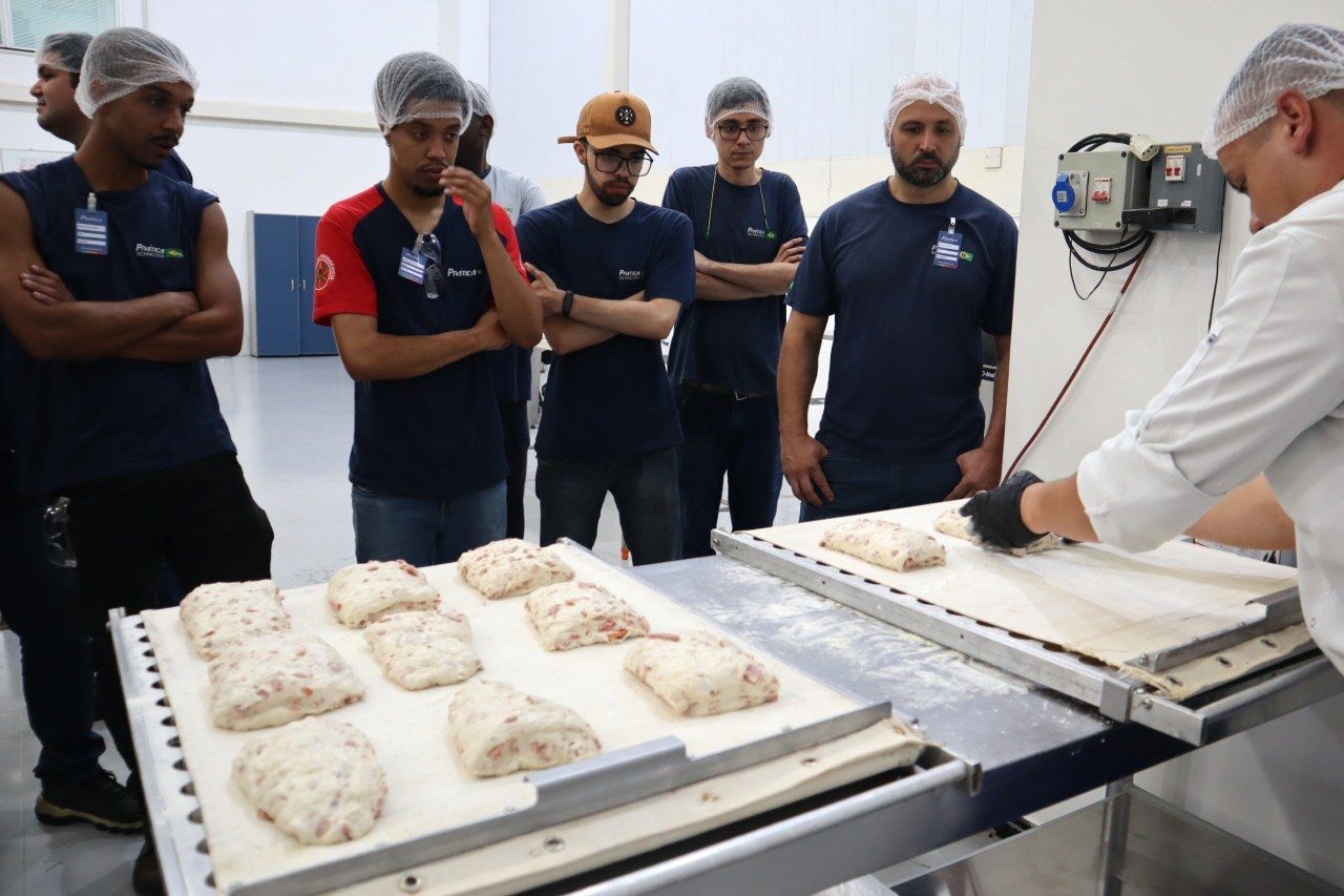 Um grupo de homens está de pé ao redor de uma mesa com pão sobre ela.