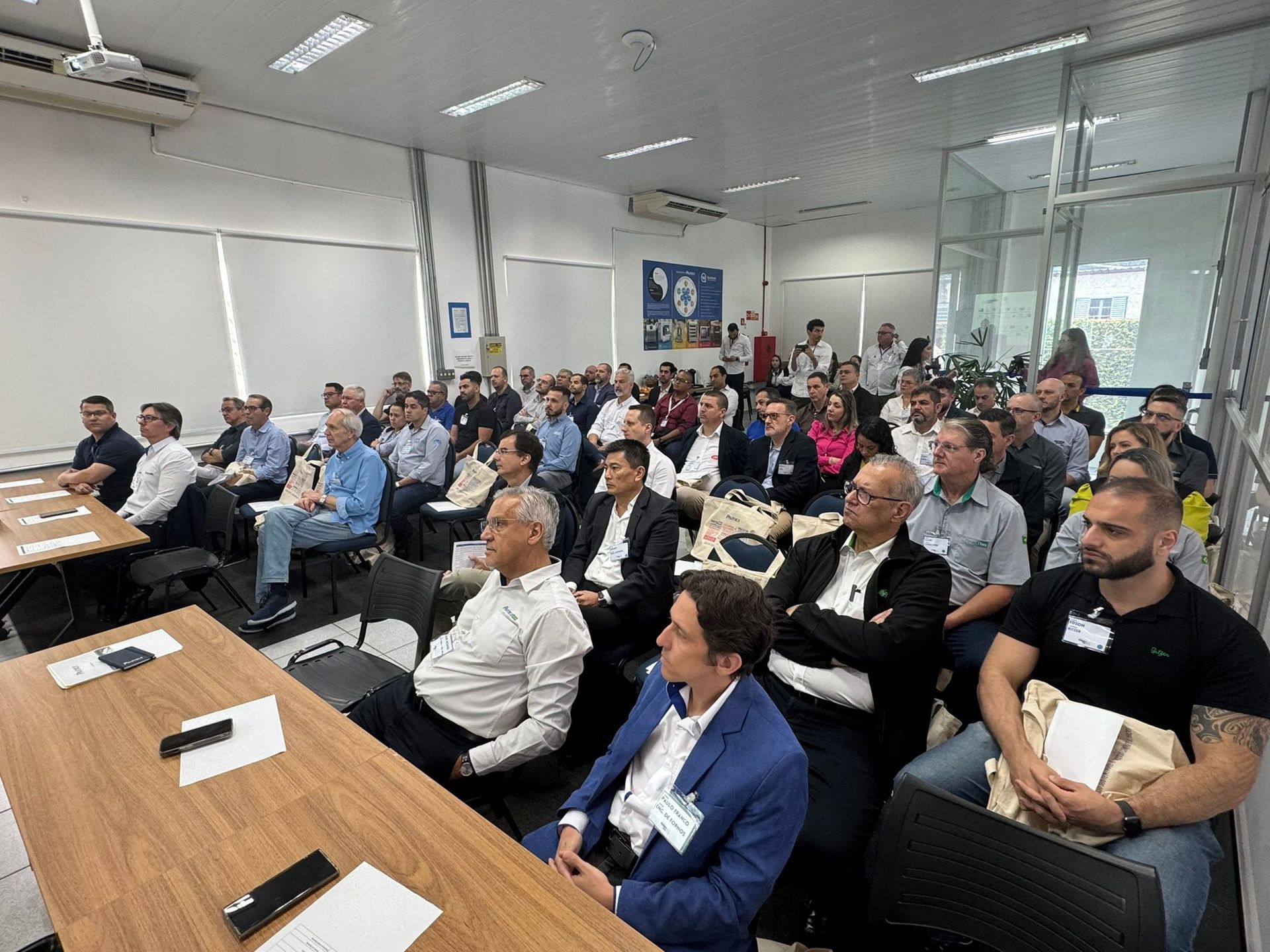 Um grande grupo de pessoas está sentado em mesas em uma sala.