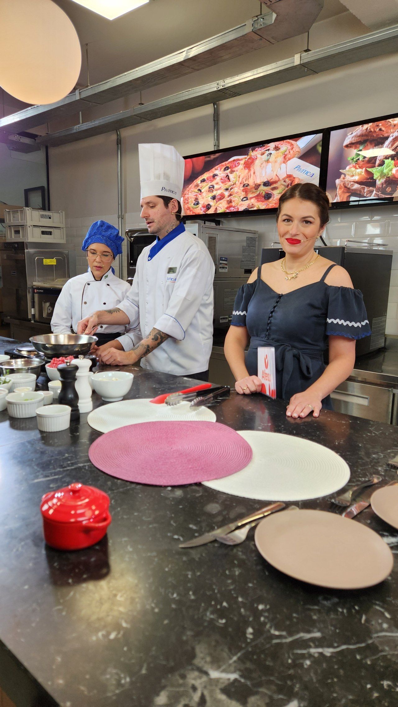 Um grupo de pessoas está em pé ao redor de uma mesa na cozinha.