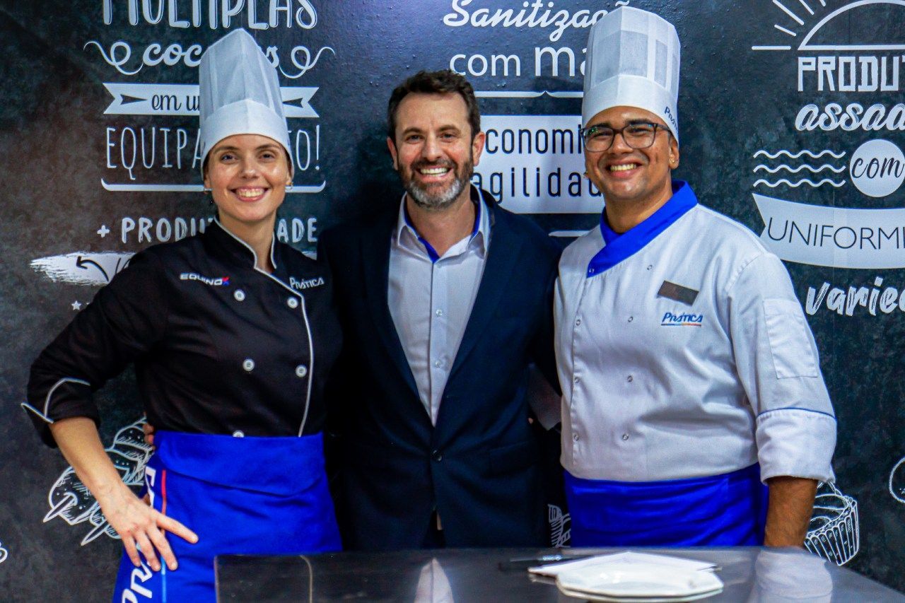 Três chefs estão posando para uma foto em frente a um quadro negro.