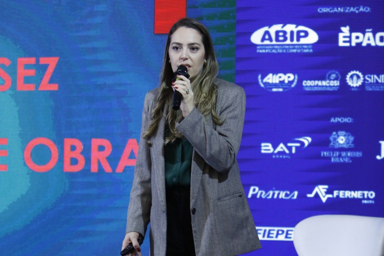 Uma mulher está falando em um microfone em frente a uma placa que diz abip