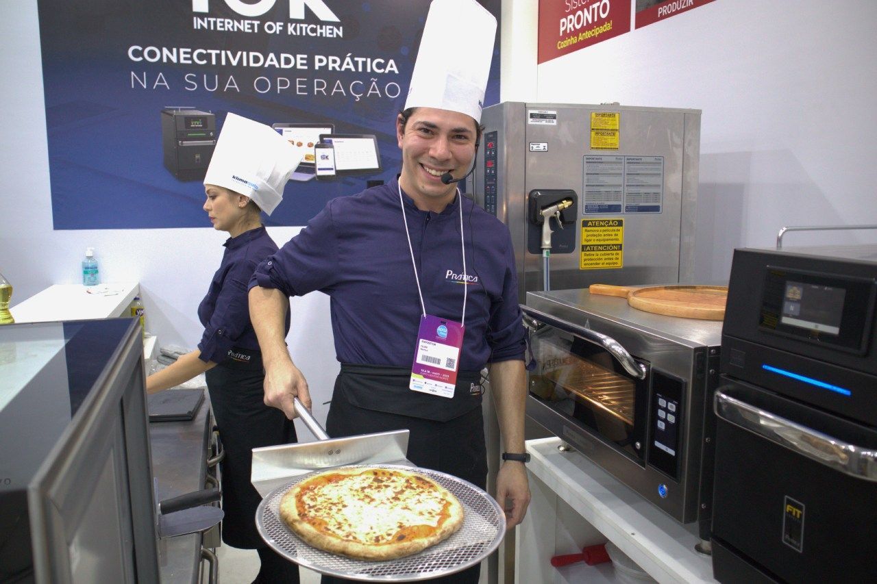 Um homem com chapéu de chef está segurando uma pizza em frente ao forno.